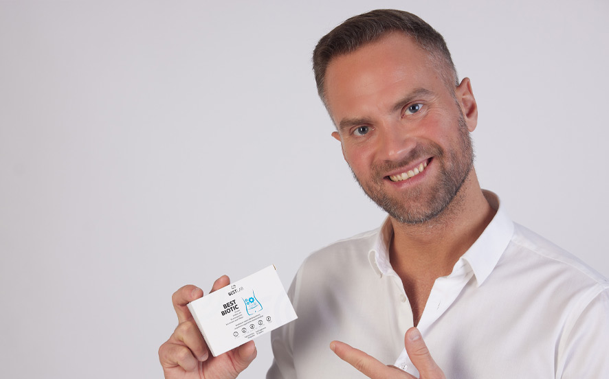 Smiling man in a white shirt holds and points to a product box labelled "Uber Bottle" against a plain white background. UK