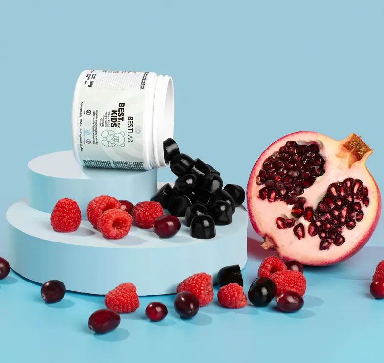 A white jar of berry gummies spills black gummies onto blue podiums, surrounded by raspberries, cranberries, and a halved pomegranate on a light blue background. UK