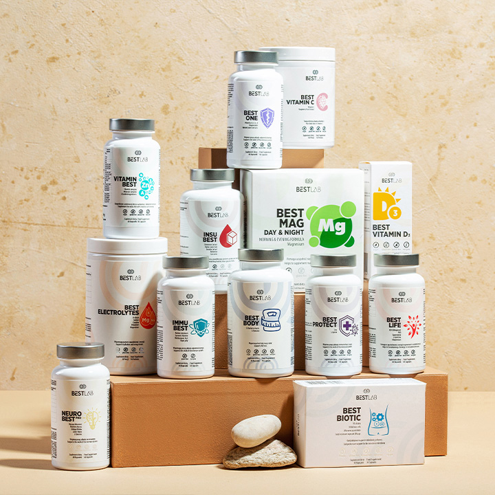 A variety of BESTLAB supplement bottles and boxes are arranged on tan steps and blocks with stones in front, displayed against a beige textured background. UK
