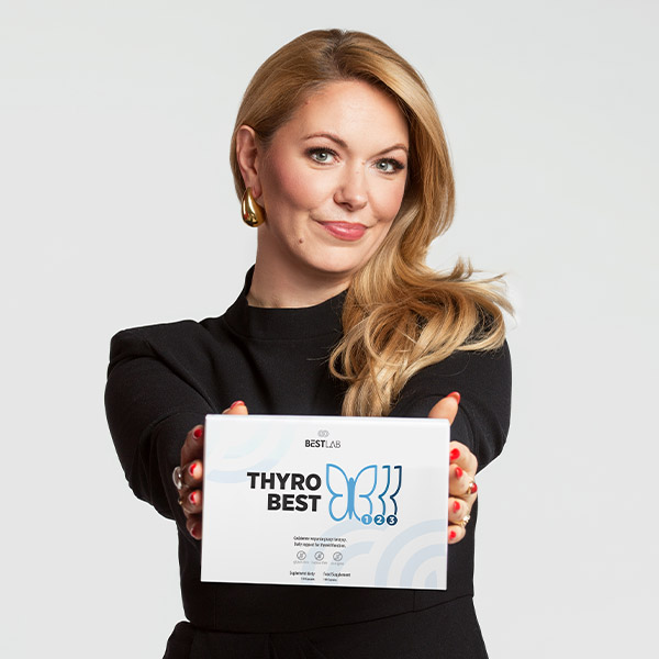 A woman with long blonde hair, wearing a black outfit, holds a box labelled THYRO BEST with a blue butterfly graphic and smiles at the camera against a plain, light background. UK