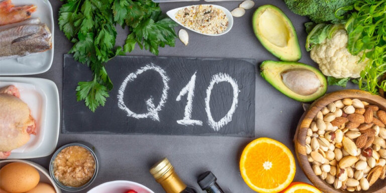 a blackboard with q10 written on it is surrounded by various healthy foods, including fish, chicken, eggs, avocado, nuts, orange segments, broccoli, cauliflower, parsley, grains, and green leafy vegetables. uk