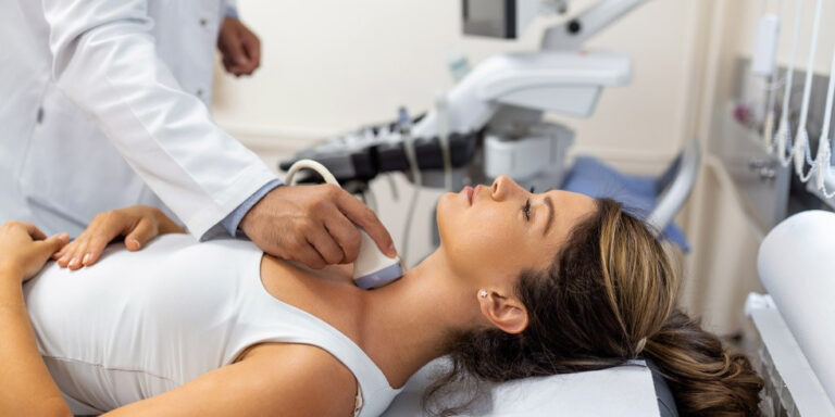 a doctor performs an ultrasound scan on a woman’s neck as she lies on an examination couch in a medical clinic. uk