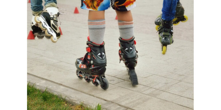 three people rollerblading outdoors; only their legs and skates are visible. one person wears grey and black skates with striped socks, whilst the others have rollerblades with yellow and white wheels. orange cones are in the background. uk