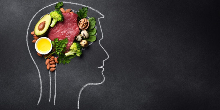 a chalk outline of a human head is filled with healthy foods, including raw steak, avocado, eggs, broccoli, nuts, and greens, symbolising the importance of nutrition for brain health on a blackboard background. uk