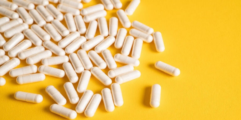 scattered white capsules on a bright yellow surface, with most of the capsules grouped in the upper left area and a few spread out towards the lower right. uk