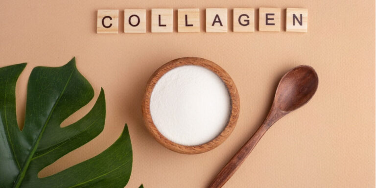 a bowl of white collagen powder next to a wooden spoon and a large green leaf, with the word collagen spelt out in wooden letter tiles above them on a beige background. uk