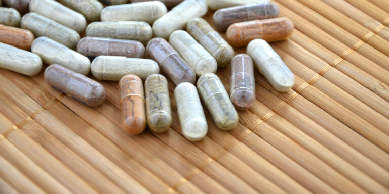 a variety of multicoloured herbal supplement capsules scattered on a bamboo mat. uk