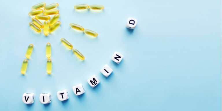 yellow vitamin d capsules are arranged in the shape of a sun on a light blue background, with lettered cubes below spelling out vitamin d. uk