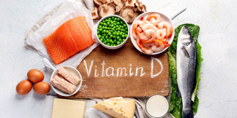 various foods rich in vitamin d, including salmon, prawns, eggs, peas, cheese, mushrooms, milk, and a whole fish, arranged around a chopping board labelled vitamin d. uk