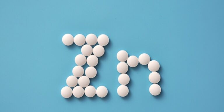 white round tablets arranged to form the letters zn on a blue background, representing the chemical symbol for zinc. uk