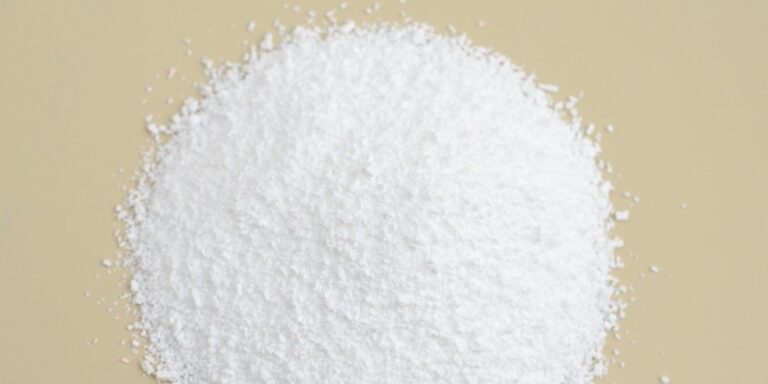 a mound of fine white powder is piled on a smooth, beige surface, with scattered granules around the edges. uk