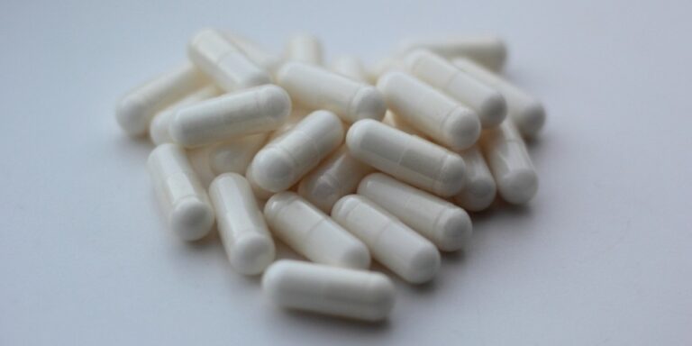 a pile of white, opaque capsules is scattered on a smooth, light coloured surface. uk