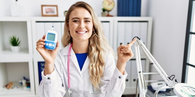 a smiling doctor in a white coat holds a glucose metre in one hand and points with the other in a bright medical surgery. uk